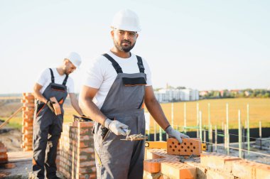 Hintli inşaat işçileri bir tuğla ev inşaatında çalışıyorlar. Bir tuğla duvar inşaatı.