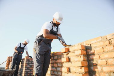 Önlüklü ve kasklı Hintli inşaat işçileri bir duvar örüyor..