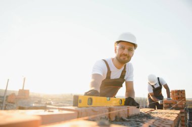 Construction worker man in work clothes and a construction helmet. Portrait of positive male builder in hardhat working at construction site.