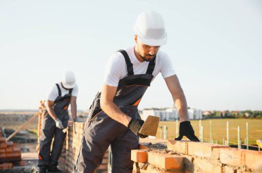 Construction worker man in work clothes and a construction helmet. Portrait of positive male builder in hardhat working at construction site.