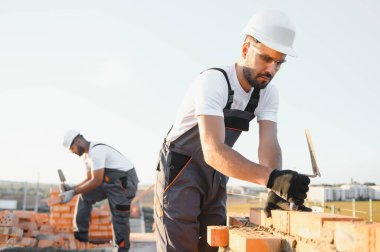 Construction worker man in work clothes and a construction helmet. Portrait of positive male builder in hardhat working at construction site.