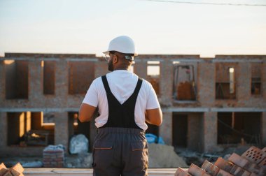 Hintli bir inşaat işçisinin portresi. Tulumlu ve inşaat alanında kasketli..