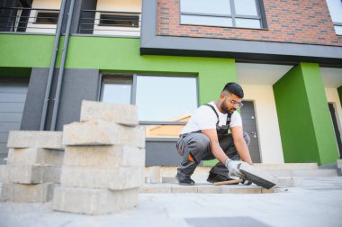 Hintli İşçi ustalıkla kaldırım taşı döşeyip çekiç kullanıyor ve eldiven takıyor..