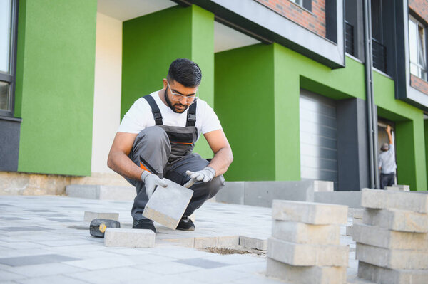 Indian Worker skillfully laying paving stones using a hammer and wearing gloves, showcasing precision.