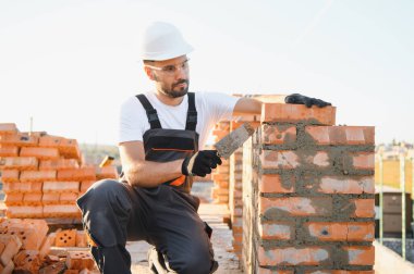 Tuğla duvar kuruluyor. Üniformalı inşaat işçisi ve güvenlik ekipmanı inşaatında çalışıyor.