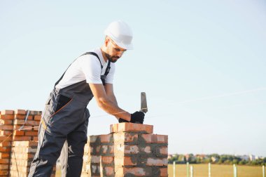 Construction worker man in work clothes and a construction helmet. Portrait of positive male builder in hardhat working at construction site.