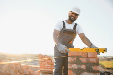 Tuğla duvar kuruluyor. Üniformalı inşaat işçisi ve güvenlik ekipmanı inşaatında çalışıyor.