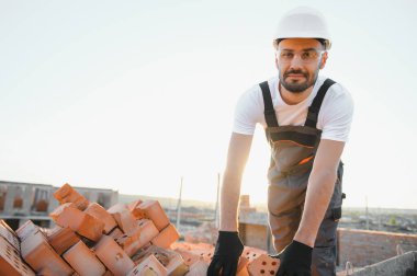 Tuğla duvar kuruluyor. Üniformalı inşaat işçisi ve güvenlik ekipmanı inşaatında çalışıyor.