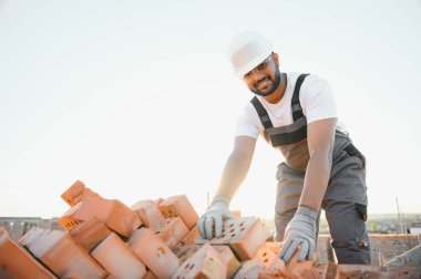 Hintli bir inşaat işçisinin portresi. Tulumlu ve inşaat alanında kasketli..