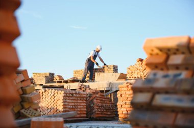 Tuğla duvar kuruluyor. Üniformalı inşaat işçisi ve güvenlik ekipmanı inşaatında çalışıyor.