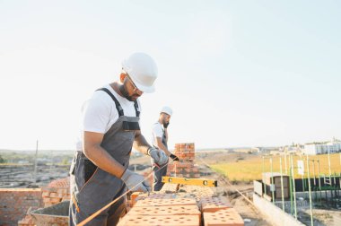 Önlüklü ve kasklı Hintli inşaat işçileri bir duvar örüyor..