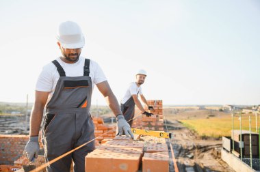 Önlüklü ve kasklı Hintli inşaat işçileri bir duvar örüyor..