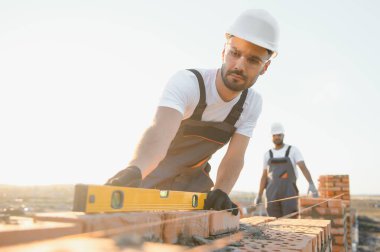 Construction worker man in work clothes and a construction helmet. Portrait of positive male builder in hardhat working at construction site.