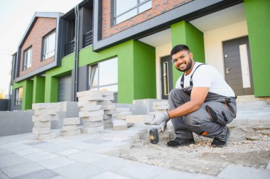 Eldivenli Hintli usta katman katman taş döşüyordu. Profesyonel kaldırım işçisi tarafından kaldırım taşı döşenmiş. Kum temeli üzerine ev avlusunda gri beton döşeme döşeme döşeme döşeme.