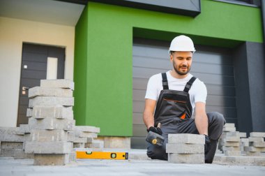 Eldivenlerin ustası katman katman taş döşüyordu. Profesyonel kaldırım işçisi tarafından kaldırım taşı döşenmiş. Kum temeli üzerine ev avlusunda gri beton döşeme döşeme döşeme döşeme.