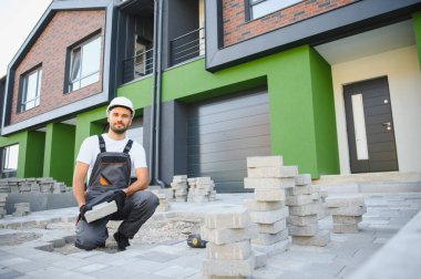 Eldivenlerin ustası katman katman taş döşüyordu. Profesyonel kaldırım işçisi tarafından kaldırım taşı döşenmiş. Kum temeli üzerine ev avlusunda gri beton döşeme döşeme döşeme döşeme.