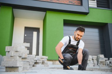 Eldivenlerin ustası katman katman taş döşüyordu. Profesyonel kaldırım işçisi tarafından kaldırım taşı döşenmiş. Kum temeli üzerine ev avlusunda gri beton döşeme döşeme döşeme döşeme.