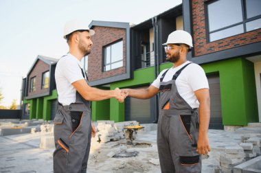 Two builders on the background of new cottages. The work is done. clipart