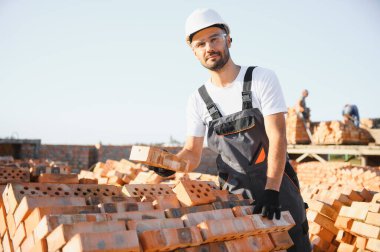 Construction worker man in work clothes and a construction helmet. Portrait of positive male builder in hardhat working at construction site.