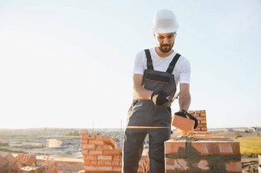 Construction worker man in work clothes and a construction helmet. Portrait of positive male builder in hardhat working at construction site.