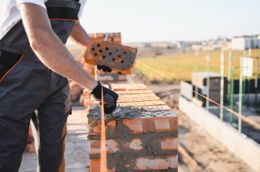 Tuğla duvar kuruluyor. Üniformalı inşaat işçisi ve güvenlik ekipmanı inşaatında çalışıyor.