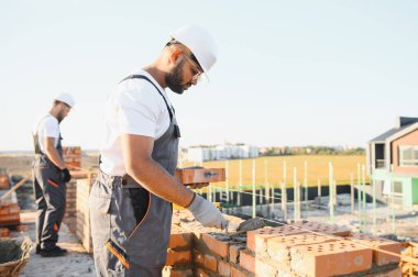 Önlüklü ve kasklı Hintli inşaat işçileri bir duvar örüyor..