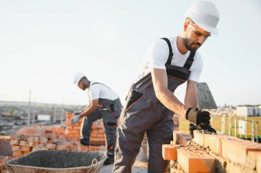 Construction worker man in work clothes and a construction helmet. Portrait of positive male builder in hardhat working at construction site.