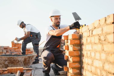 Construction worker man in work clothes and a construction helmet. Portrait of positive male builder in hardhat working at construction site.