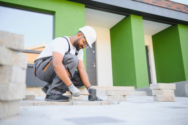 Eldivenli Hintli usta katman katman taş döşüyordu. Profesyonel kaldırım işçisi tarafından kaldırım taşı döşenmiş. Kum temeli üzerine ev avlusunda gri beton döşeme döşeme döşeme döşeme.