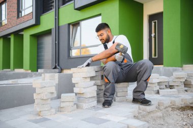 Eldivenli Hintli usta katman katman taş döşüyordu. Profesyonel kaldırım işçisi tarafından kaldırım taşı döşenmiş. Kum temeli üzerine ev avlusunda gri beton döşeme döşeme döşeme döşeme.