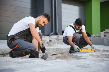 Bir grup çok ırklı işçi bir evin yakınındaki kaldırıma taş döşedi..