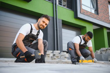Bir grup çok ırklı işçi bir evin yakınındaki kaldırıma taş döşedi..