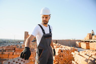 Construction worker man in work clothes and a construction helmet. Portrait of positive male builder in hardhat working at construction site.