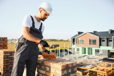 Construction worker man in work clothes and a construction helmet. Portrait of positive male builder in hardhat working at construction site.