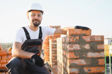 Construction worker man in work clothes and a construction helmet. Portrait of positive male builder in hardhat working at construction site.