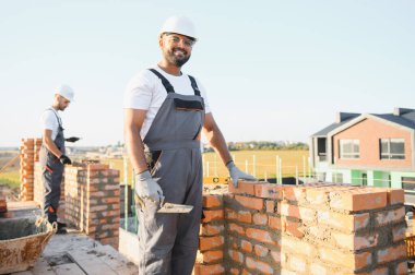 Önlüklü ve kasklı Hintli inşaat işçileri bir duvar örüyor..
