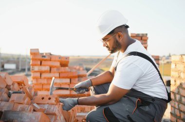 Tuğla duvar kuruluyor. Üniformalı inşaat işçisi ve güvenlik ekipmanı inşaatında çalışıyor.