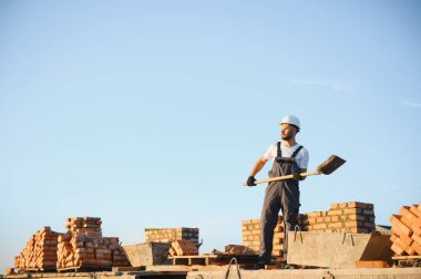 Construction worker man in work clothes and a construction helmet. Portrait of positive male builder in hardhat working at construction site.