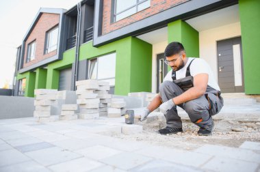 Hintli İşçi ustalıkla kaldırım taşı döşeyip çekiç kullanıyor ve eldiven takıyor..