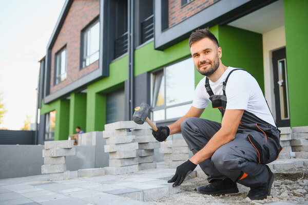 Worker skillfully laying paving stones using a hammer and wearing gloves, showcasing precision.