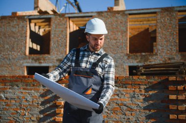 Tuğladan evler inşa eden bir mimar ya da mühendis inşaat planını elinde tutuyor ve işlerin nasıl yürüdüğünü kontrol ediyor..