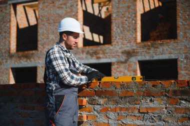 Tuğla duvar kuruluyor. Üniformalı inşaat işçisi ve güvenlik ekipmanı inşaatında çalışıyor.