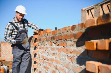 Tuğla duvar kuruluyor. Üniformalı inşaat işçisi ve güvenlik ekipmanı inşaatında çalışıyor.