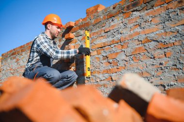 Tuğla duvar kuruluyor. Üniformalı inşaat işçisi ve güvenlik ekipmanı inşaatında çalışıyor.
