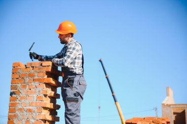 Tuğla duvar kuruluyor. Üniformalı inşaat işçisi ve güvenlik ekipmanı inşaatında çalışıyor.