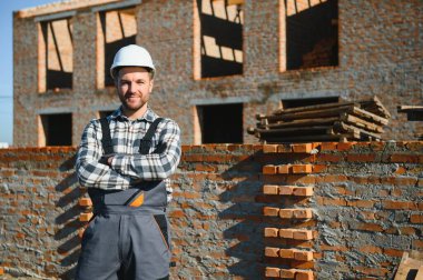 Tuğla duvar kuruluyor. Üniformalı inşaat işçisi ve güvenlik ekipmanı inşaatında çalışıyor.