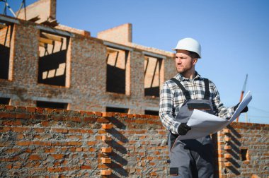 Tuğla duvar kuruluyor. Üniformalı inşaat işçisi ve güvenlik ekipmanı inşaatında çalışıyor.