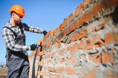 Tuğla duvar kuruluyor. Üniformalı inşaat işçisi ve güvenlik ekipmanı inşaatında çalışıyor.