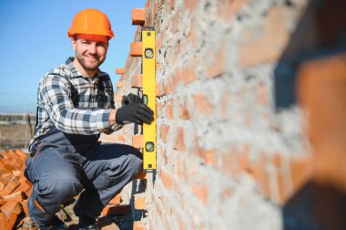 Yeni kırmızı tuğla duvar açık kontrol etmek için bir ruh düzeyi kullanarak Duvarcı ustası. Örmek temelleri duvar örgü teknikleri.