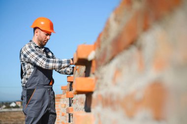 Tuğla duvar kuruluyor. Üniformalı inşaat işçisi ve güvenlik ekipmanı inşaatında çalışıyor.